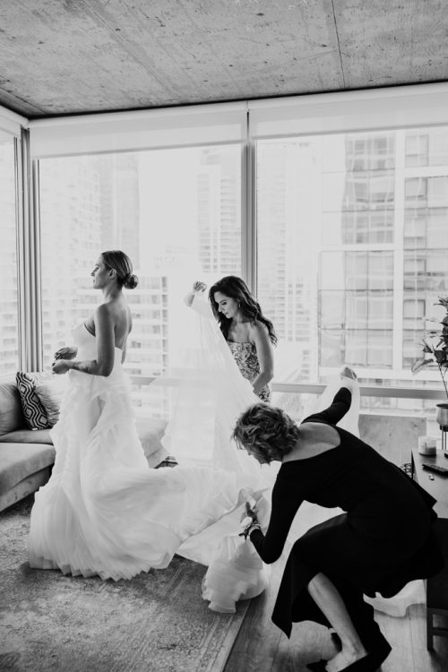 Black and white photo of bride's mother and bridesmaid helping with bride's dress before Bond Chapel wedding in Chicago
