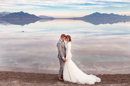 Romantic wedding photo of bride and groom at sunrise with mountain view at Bonneville Salt Flats in Utah