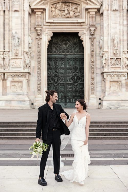 Candid photo of bride and groom walking in front of Milan Cathedral after their morning Italy elopement