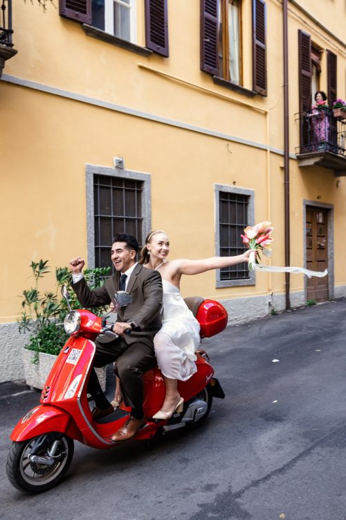 Just eloped bride and groom ride on red Vespa through streets of Italy