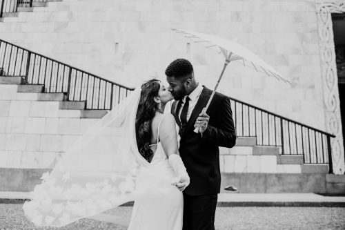 Romantic photo of bride and groom kissing under parasol with flowing veil at their Museo 900 wedding in Milan, Italy