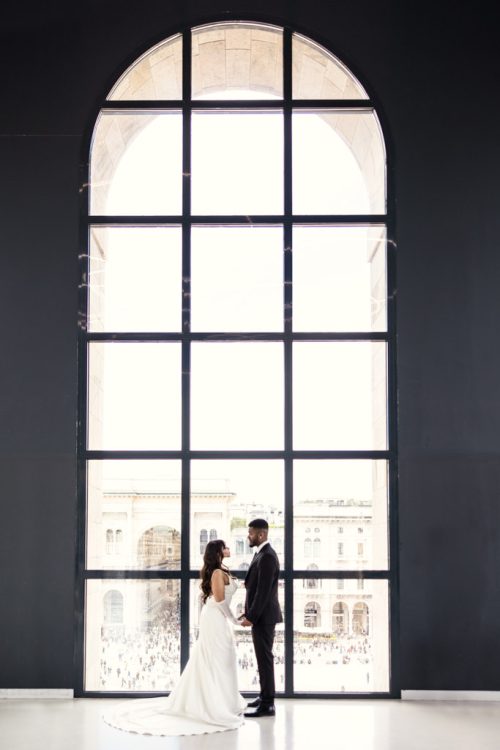 Creative photo of bride and groom standing in arched window at Museo del Novecento in downtown Milan