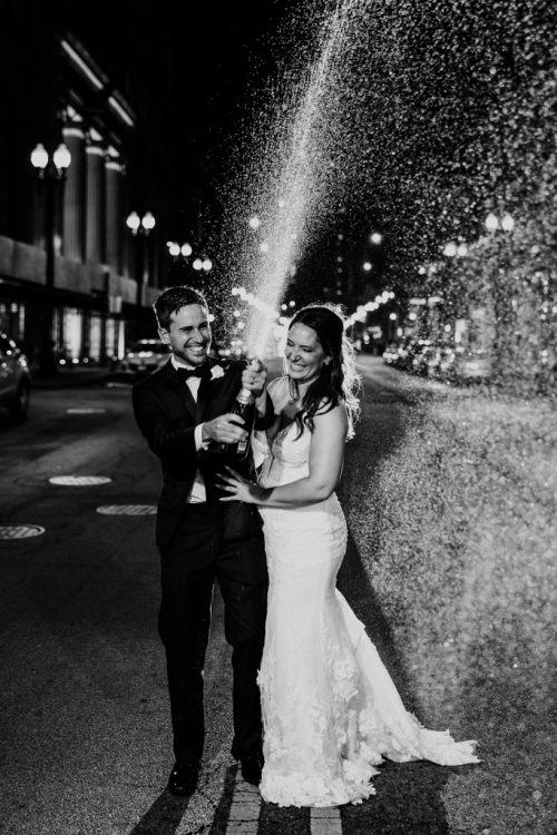 Happy newlyweds pop a bottle of champagne in the street at their 190 S. LaSalle Chicago wedding