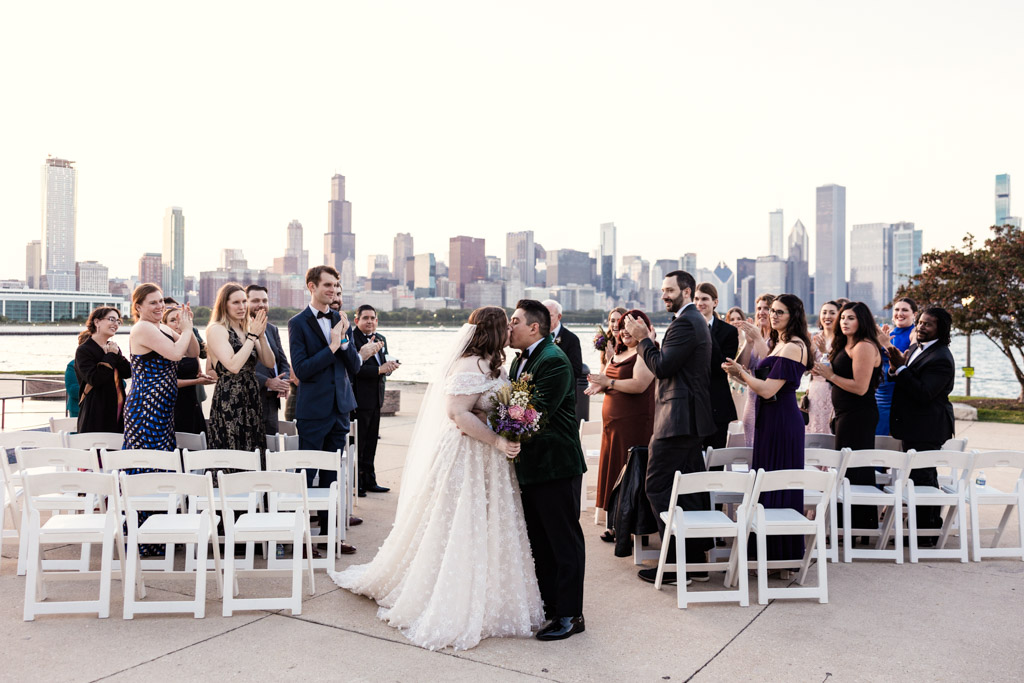 Just married bride and groom kiss while guests applaud during their Adler Planetarium wedding ceremony at sunset