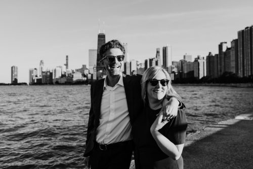 Black and white photo of engaged couple wearing sunglasses on the lakeshore at North Avenue Beach during Chicago engagement session