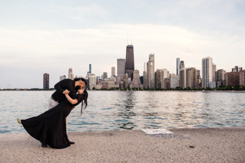Couple dips and kisses in front of Chicago skyline at their summer North Avenue Beach engagement session