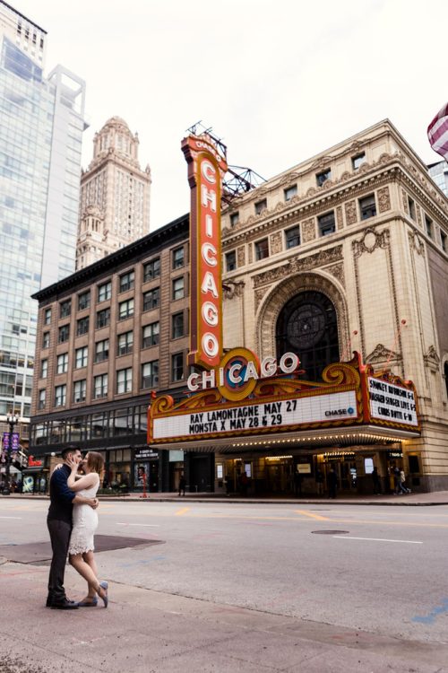 Downtown Chicago engagement photo of couple kissing in street in front of Chicago Theatre sign