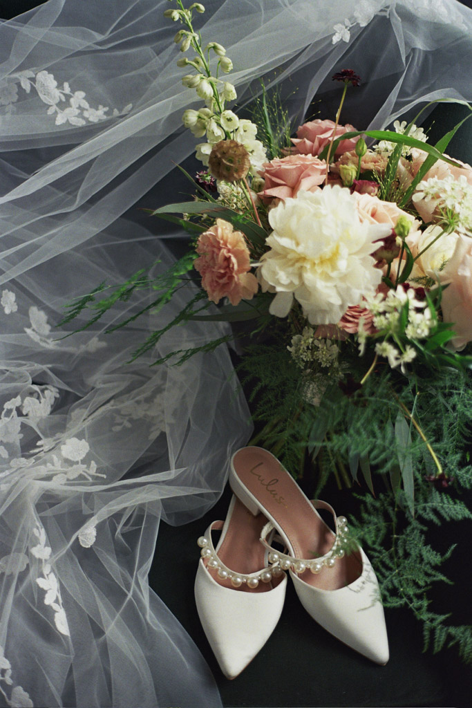 Bride's shoes and spring floral bouquet sit on green velvet chair with embroidered veil at Pendry Chicago hotel
