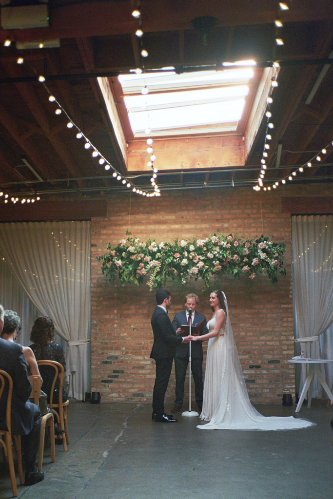 Bride and groom stand under skylight and string lights during their Arbory Chicago wedding ceremony captured on film