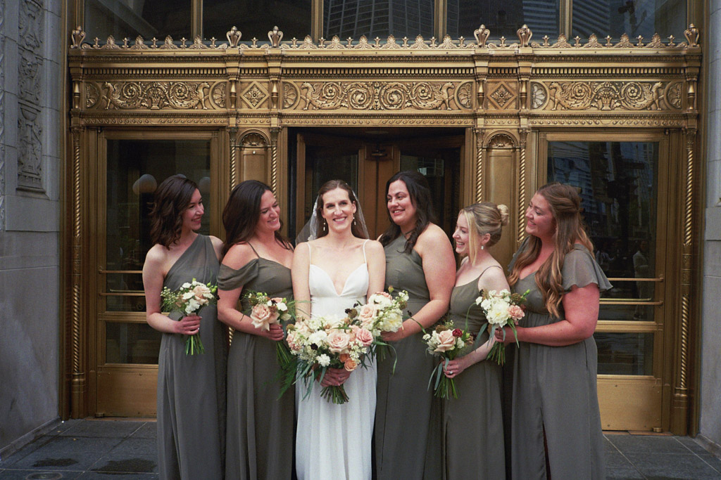 Candid photo of bride and bridesmaids laughing in front of gold doors in downtown Chicago captured on film