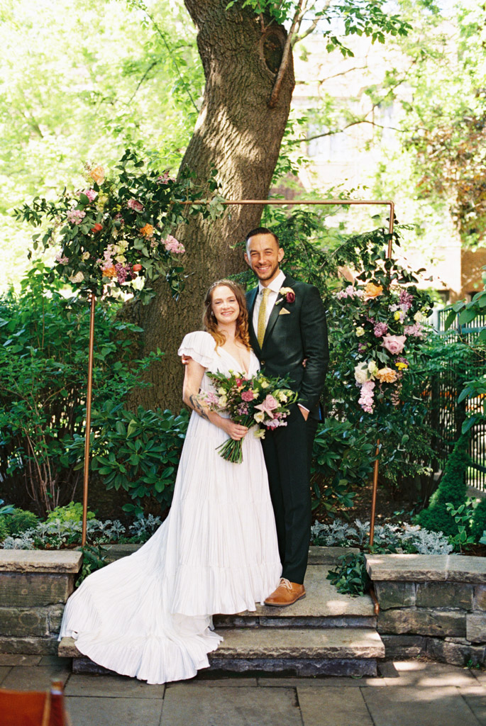 Happy newlyweds smile under colorful floral arch during spring wedding ceremony at Firehouse Chicago