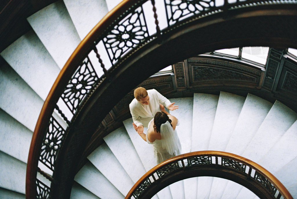 Two brides stand on spiral staircase at The Rookery Building during their first look before Chicago wedding ceremony