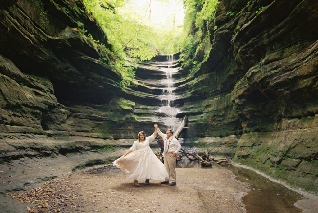 Bride and groom dance in French Canyon at Starved Rock State Park with romantic waterfall after intimate elopement