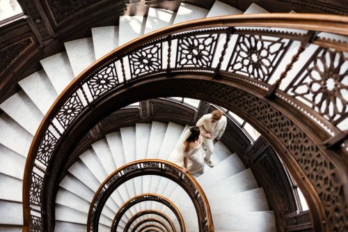 Two brides walk up spiral staircase at The Rookery building in downtown Chicago