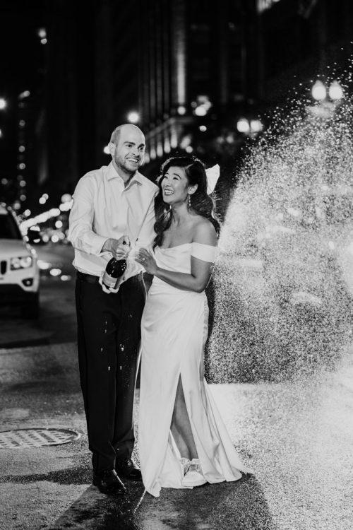 Bride and groom pop a bottle of champagne on downtown Chicago street at night