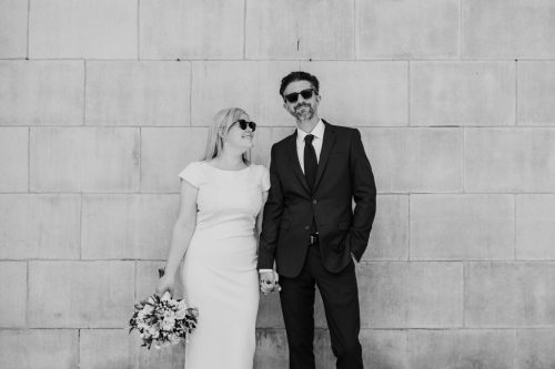 Black and white photo of bride and groom in sunglasses outside St. Mary of the Lake Catholic church after their intimate wedding ceremony