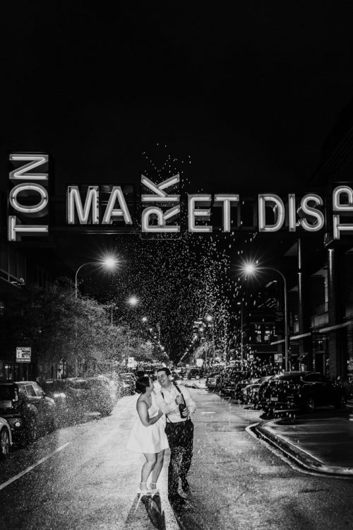 Newlywed couple dances in the rainy street at night under the Fulton Market neon sign during their Dalcy Chicago wedding reception