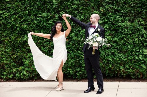 Fun photo of bride and groom dancing in front of greenery wall in Millennium Park for their Lurie Garden wedding photos