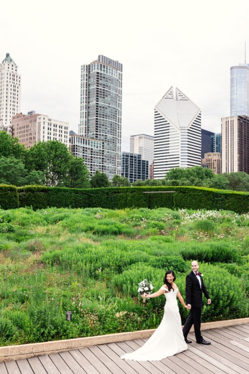 Happy bride and groom hold hands in Lurie Garden with Chicago skyline backdrop