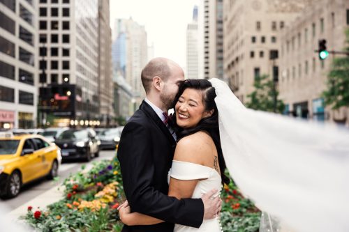 Romantic photo of bride and groom standing in middle of Michigan Avenue with flowing veil and traffic before downtown Chicago library wedding