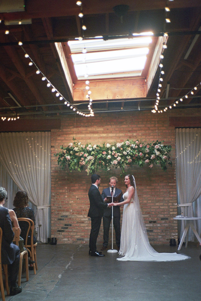 Bride and groom stand under skylight and string lights during their Arbory Chicago wedding ceremony captured on film