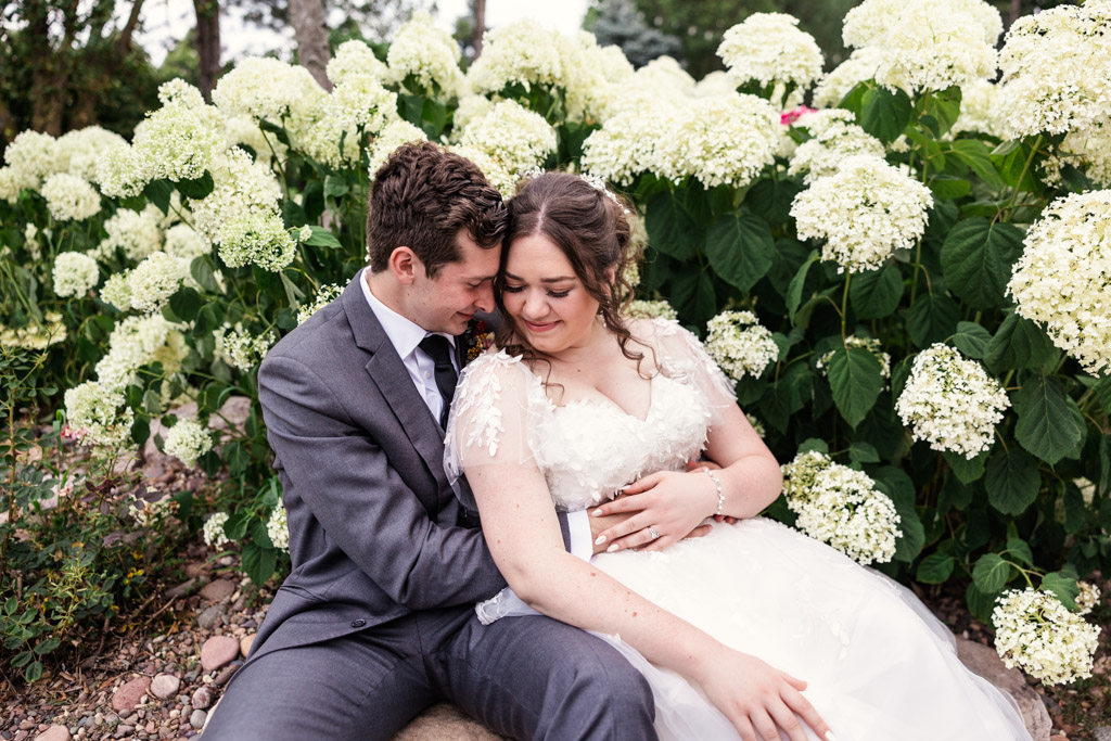 Candid photo of bride and groom surrounded by white flowers outside CD&ME