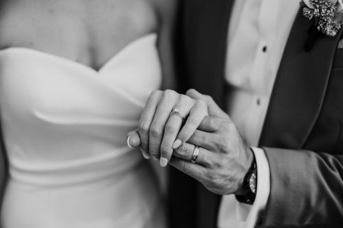 Black and white photo of bride and groom holding hands, showing wedding rings before their Cafe Brauer wedding