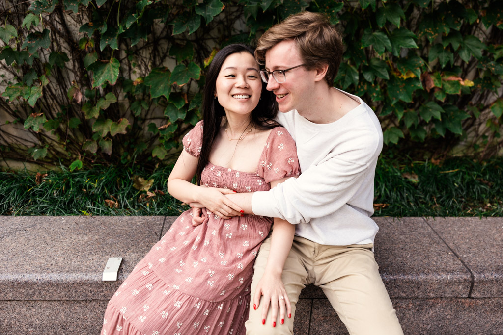 Couple holds each other while sitting on a granite ledge at the Chicago Riverwalk during sunrise engagement session