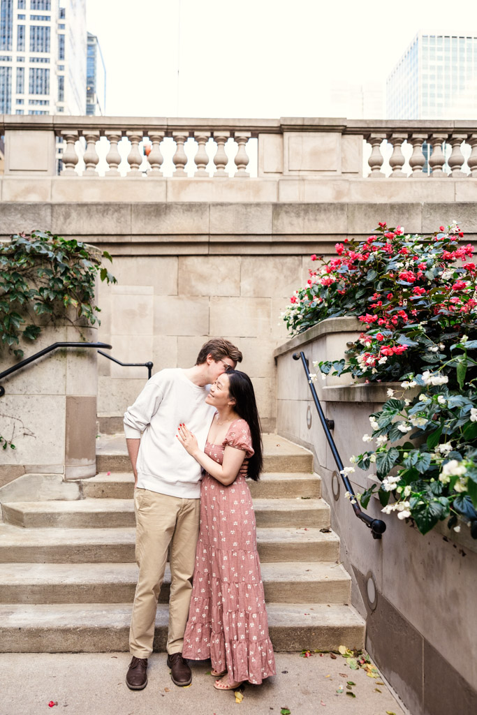 Man kisses his partner's cheek as they stand near a stone staircase on the Chicago Riverwalk