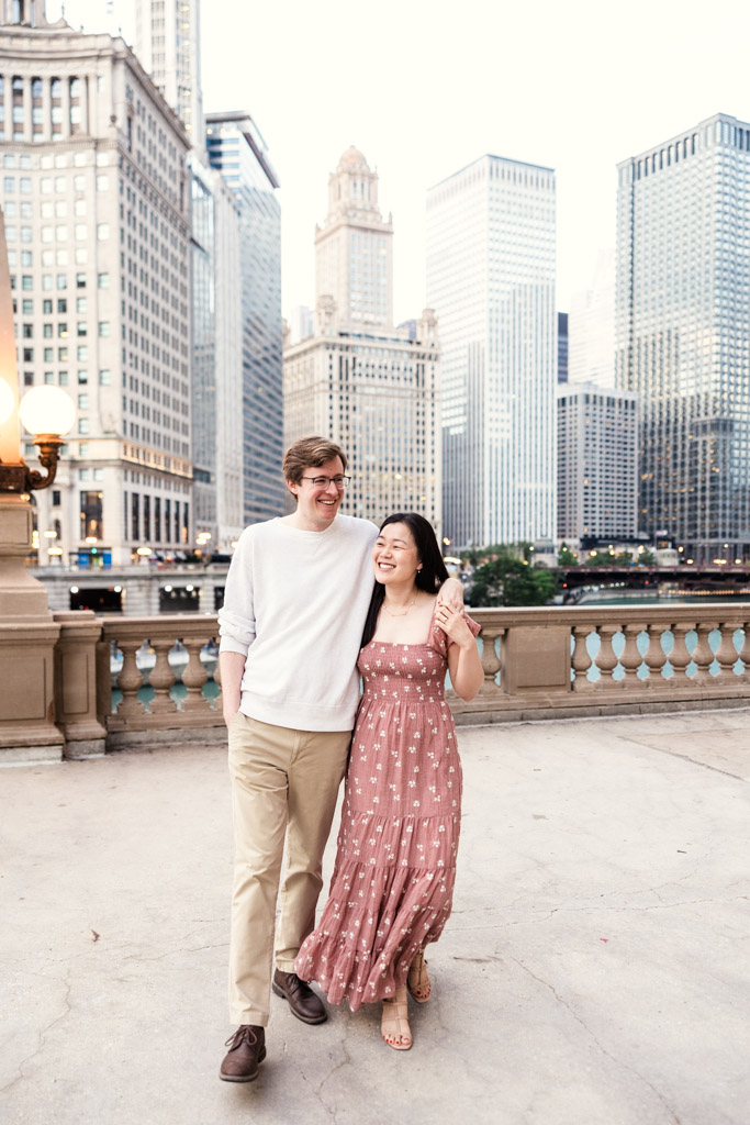 Engaged couple walks along the Chicago River with Chicago skyscrapers in the background
