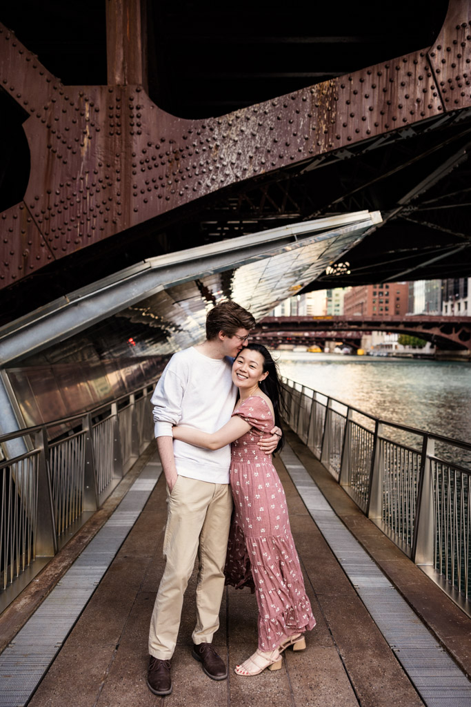 Couple holds each other beneath a bridge on the Chicago Riverwalk during sunrise engagement session