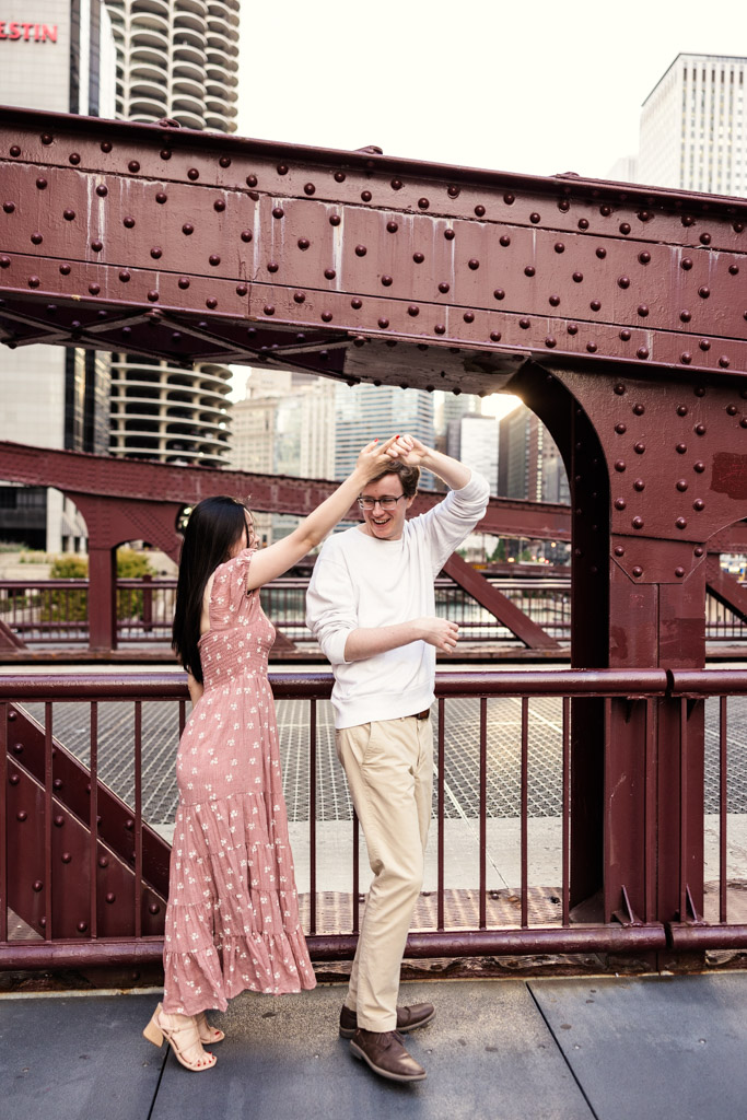Woman twirls her partner as they stand on the Clark Street Bridge during downtown Chicago engagement session