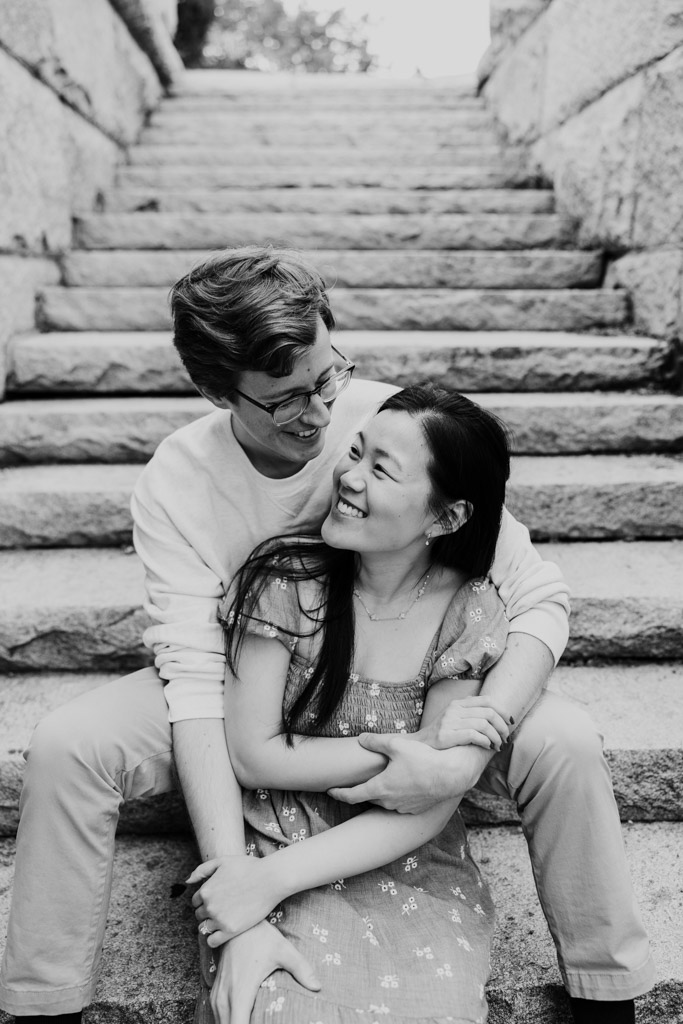 Black and white photo of smiling engaged couple sitting on stone stairs near Ulysses S. Grant Monument in Lincoln Park