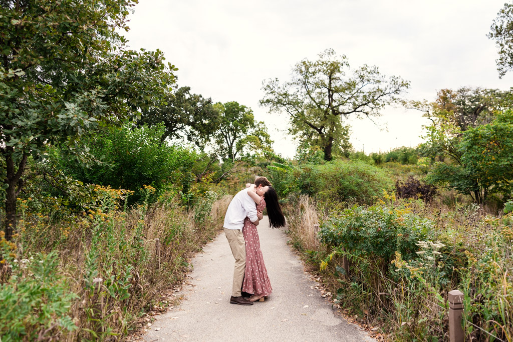 Couple embraces on a path surrounded by wildflowers during sunrise Lincoln Park engagement session
