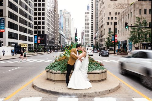 Creative photo of bride and groom kissing in the median of Michigan Ave in downtown Chicago with tall buildings and cars around them