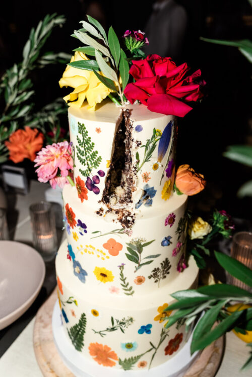 A three-tiered cake adorned with colorful flowers and a slice removed during Chicago wedding reception at The Oakville Grill and Cellar