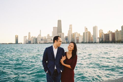 Film photo of happy engaged couple smiling on the shore of Lake Michigan, framed by Chicago skyline