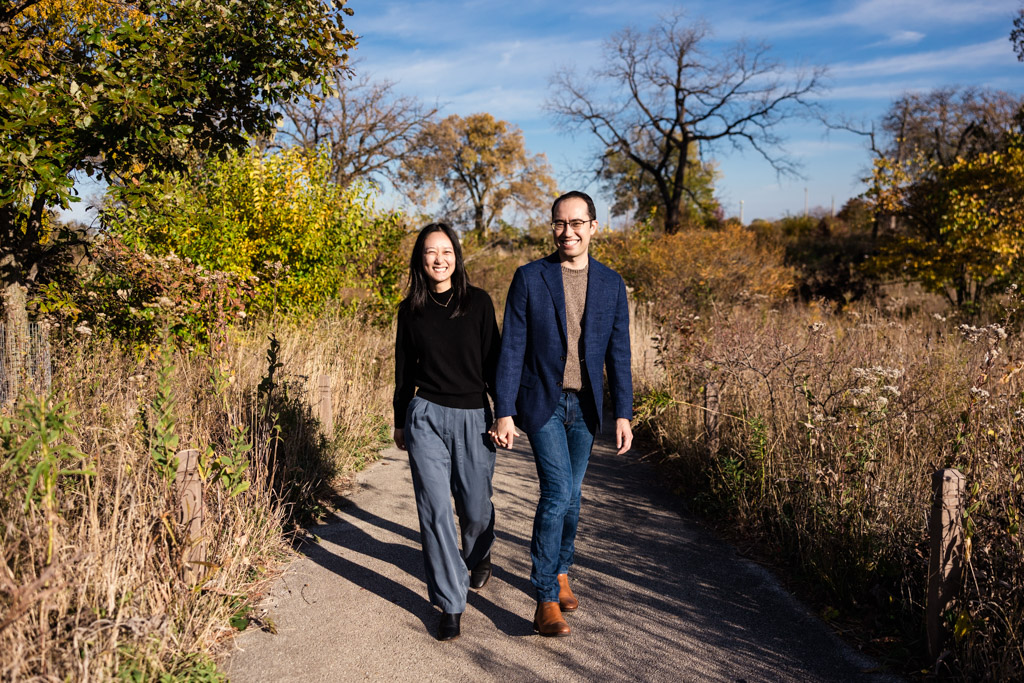 Happy engaged couple walks along Lincoln Park Nature Boardwalk with colorful foliage during their Chicago fall engagement session