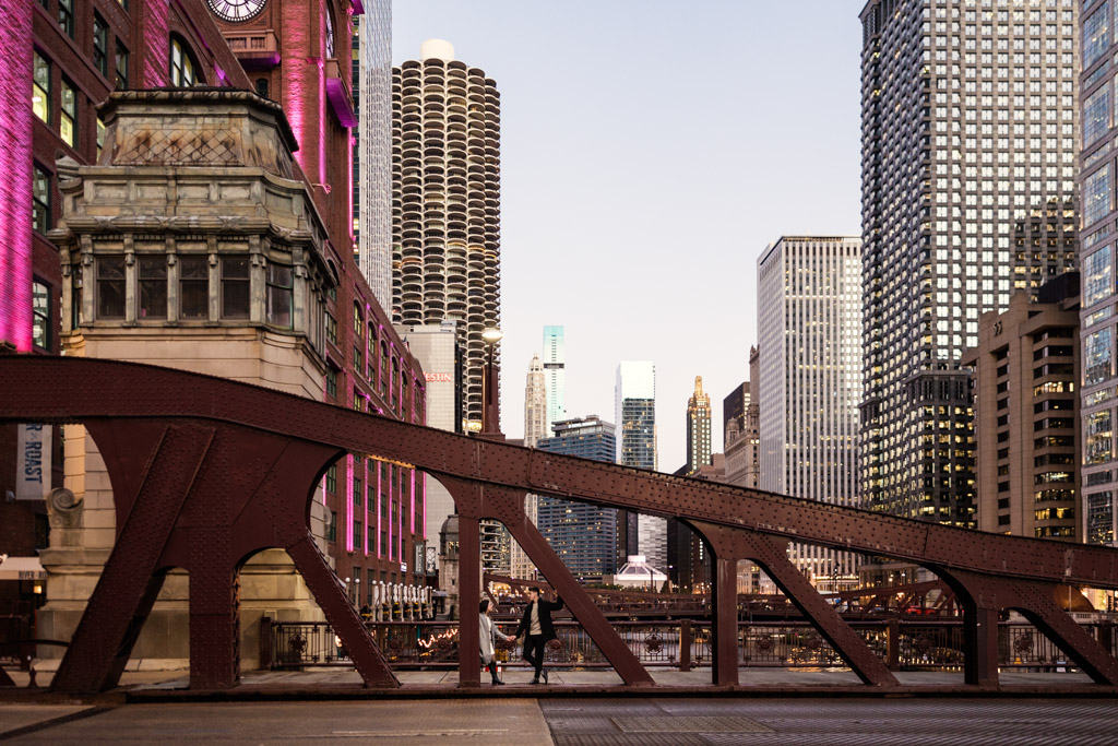 Engaged couple hangs out on the LaSalle Street Bridge in downtown Chicago with skyscrapers in the background
