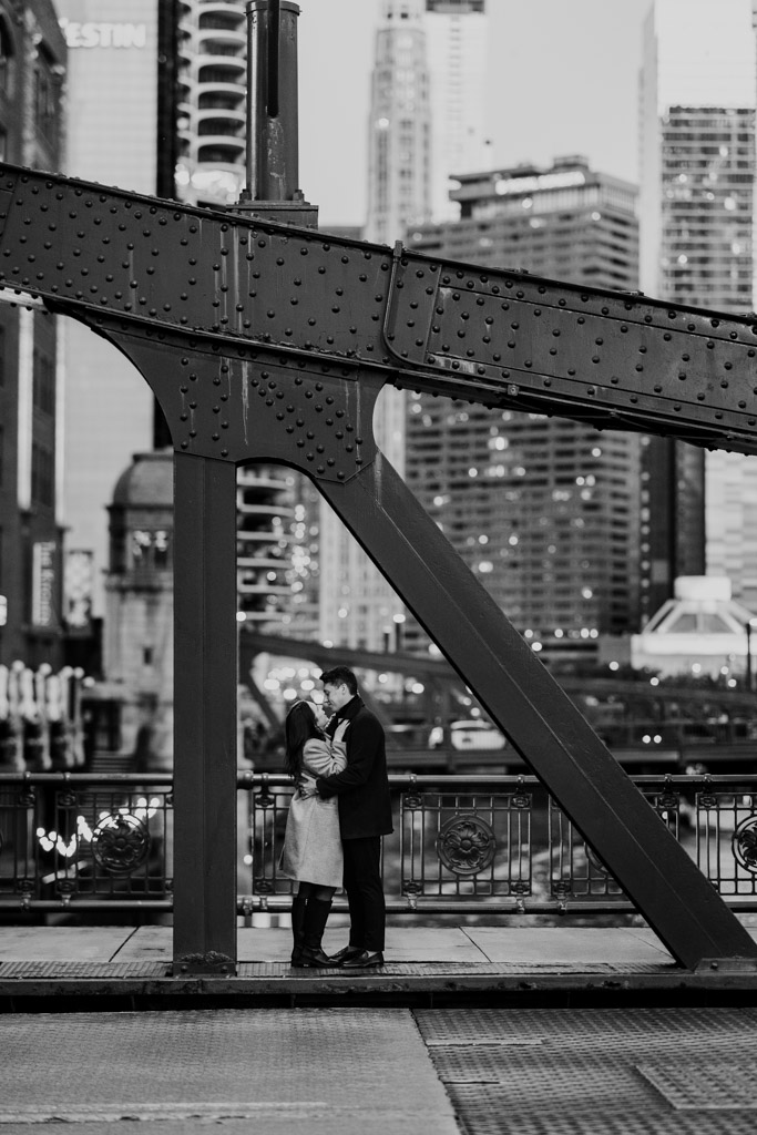 Black and white photo of couple holding each other on a downtown Chicago bridge during fall engagement session
