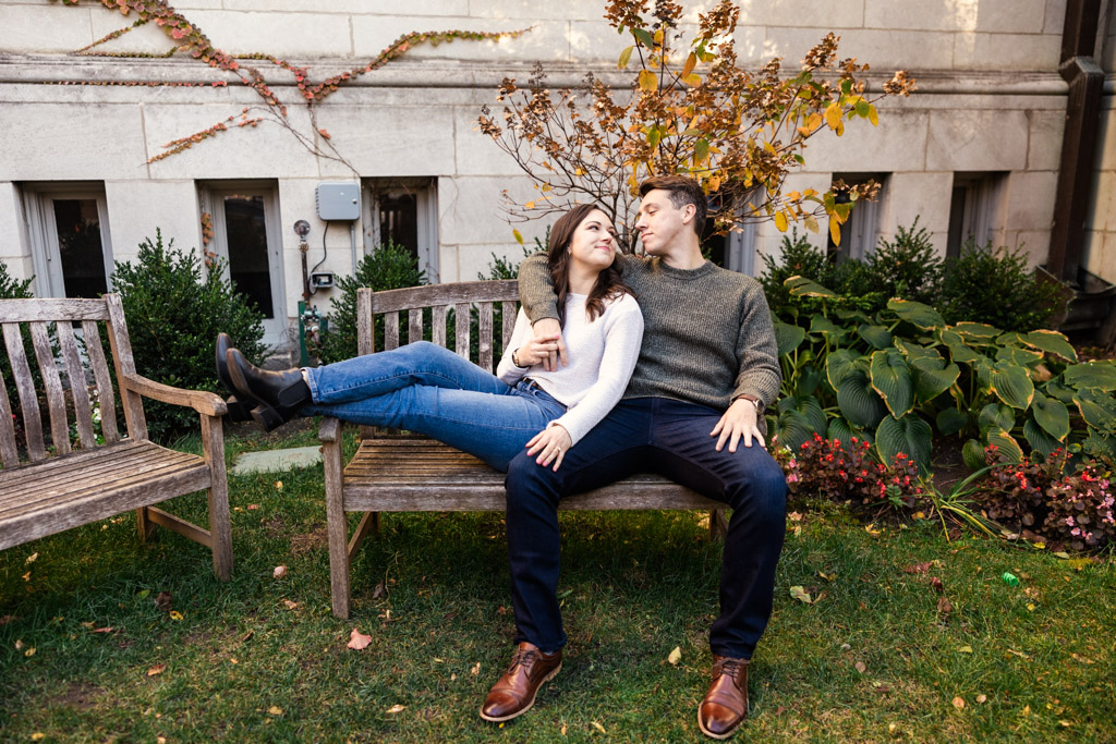 Couple sits smiling on a wooden bench in a garden during their Lincoln Park fall engagement session
