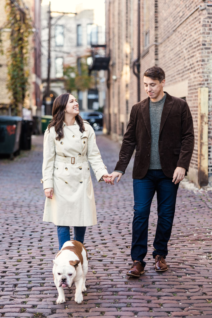 Couple walks with their bulldog on a cobblestone street during Lincoln Park fall engagement session