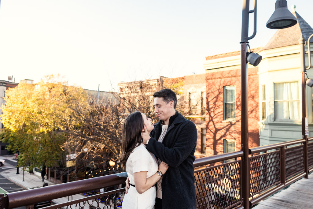 Couple embraces on a CTA platform with buildings and colorful trees in the background during their fall engagement session