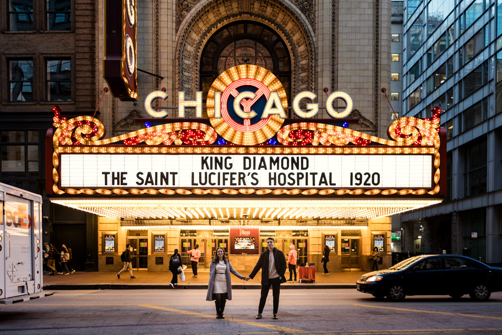 Poprtrait of engaged couple holding hands in front of the illuminated Chicago Theater marquee