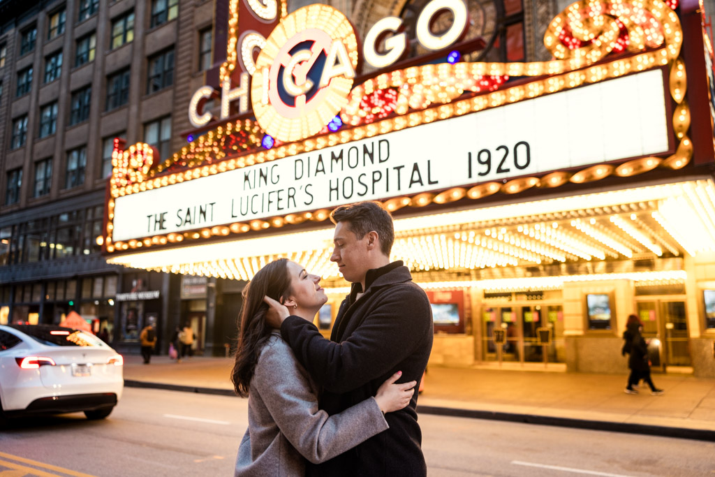 Engaged couple holds each other looking into each others' eyes in front of the brightly-lit Chicago Theatre marquee