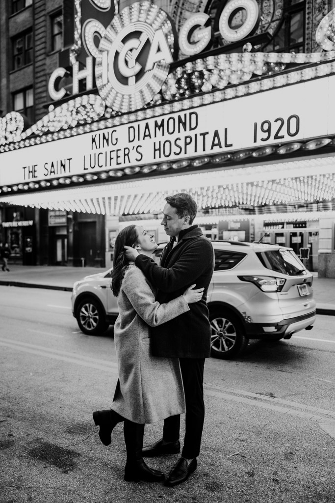Couple embraces in front of the Chicago Theater marquee with bright lights, during their downtown Chicago engagement session