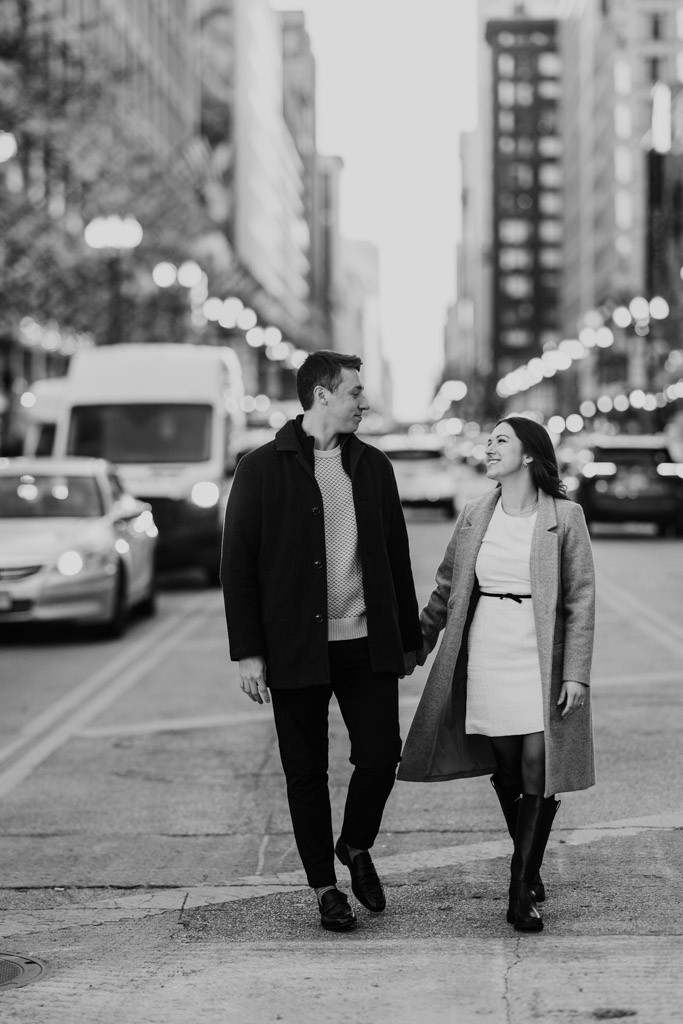 Black and white photo of couple walking hand in hand on the median of a downtown Chicago street during fall engagement session