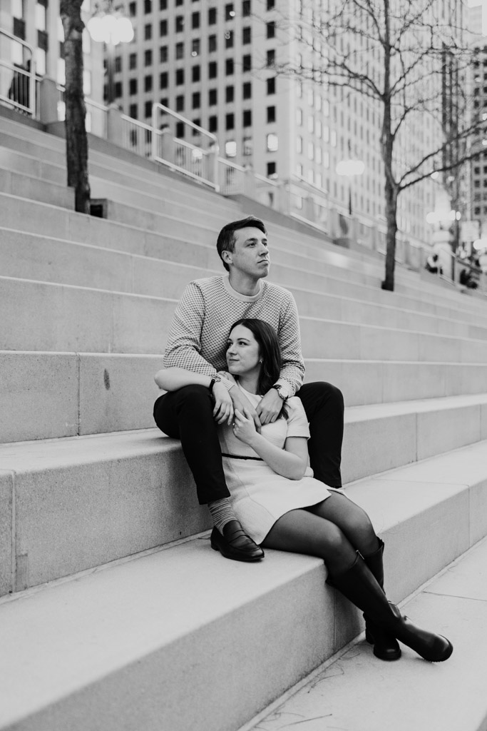 Black and white photo of engaged couple sitting on stone stairs at the Chicago Riverwalk