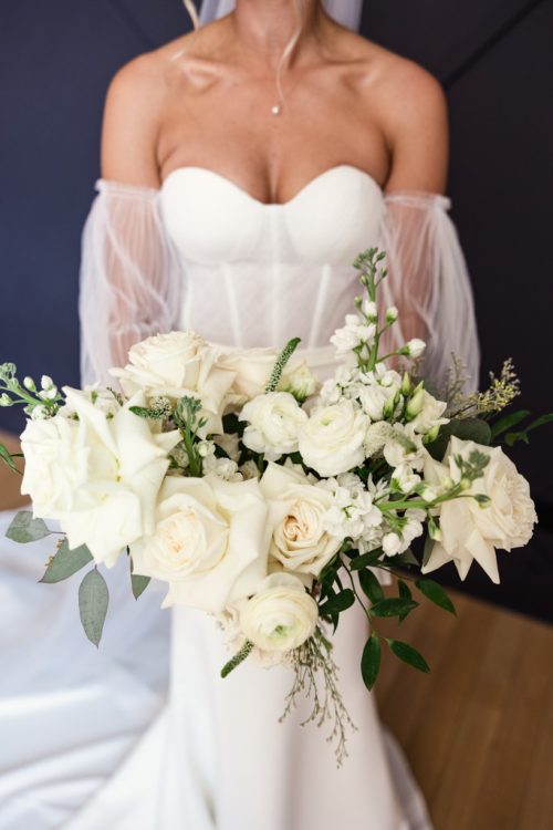 Photo of bride holding her bouquet of white flowers and greenery