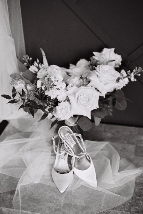 Black and white photo of bride's shoes on veil with a bouquet of roses
